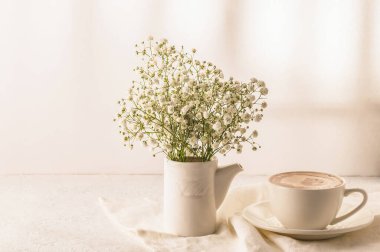 Coffee, a bouquet of gypsophila in a white vase on a white table. Cozy breakfast.