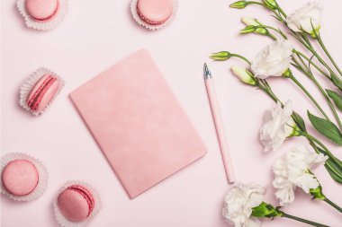 Düz kompozisyon pembe defter, badem kurabiyesi ve pembe arka planda Eustoma. Şık bir kadın işyeri. Kartpostal.