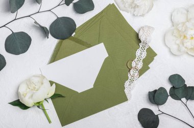 Düğün davetiyesi ya da yeşil zarflı tebrik kartı modeli, beyaz şakayık çiçekleri ve açık arkaplanda açılış kurdelesi.