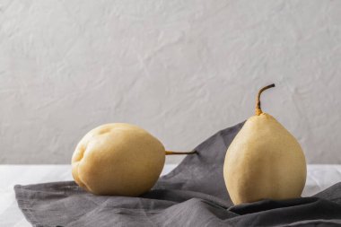 Masadaki gri peçetenin üzerinde iki tane olgun Asya armudu var..