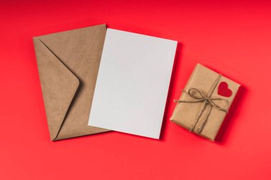 Kraft kağıt zarf, boş form ve kırmızı arka planda hediye kutusu. Sevgililer Günü veya doğum günü tebrik kartı maketi.