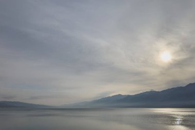 Silhouettes of misty mountains and panorama of the lake. Beautiful mountain landscape. Orto-Tokoy reservoir in Kyrgyzstan in winter. clipart