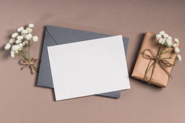 Üzerinde boş kart olan gri bir zarf ve kahverengi arka planda çigila olan bir hediye kutusu. Tebrik kartı modeli.