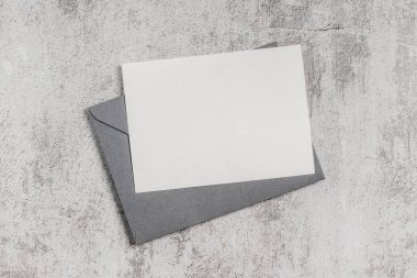 Beton zemin üzerinde boş kart olan gri bir zarf. Davetiye, tebrik kartı modeli.