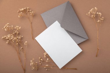 Bej kahve arka planında gri bir zarf ve kurutulmuş çigila çiçekleri. Sıcak toprak tonları. Kartpostal.
