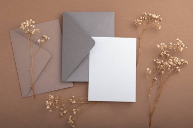 Bej arka planda gri ve kahverengimsi zarflar ve kurutulmuş çingene çiçekleri. Sıcak toprak tonları. Kartpostal.