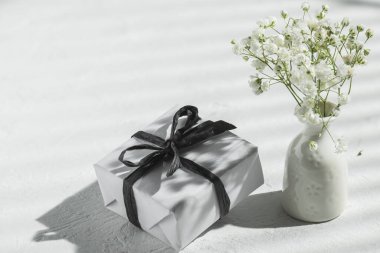 Beyaz hediye kutusu ve vazo. Güneş altında masanın üzerinde çingene resmi var. İyi tatiller..