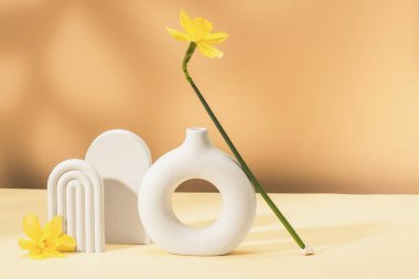 Sarı nergis, seramik vazo ve alçı figürlü şık bir kompozisyon. Parlak bahar arkaplanı, ürün sunumu. Boşluğu kopyala