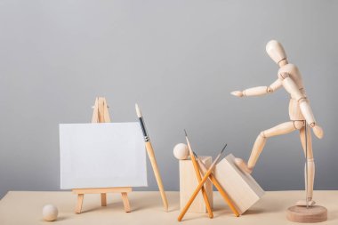Şövalenin üzerinde minyatür bir tuval, tahta bir insan figürü ve sanat fırçaları olan yaratıcı bir kompozisyon. Kopya alanı ile sanat yaratıcılığı kavramı.