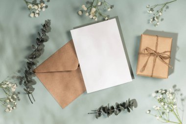 Tebrik kartı ya da düğün davetiyesi modeli. Kraft zarfı, boş antet, hediye kutusu ve zeytin arkaplanda ince dallar ve okaliptüs..