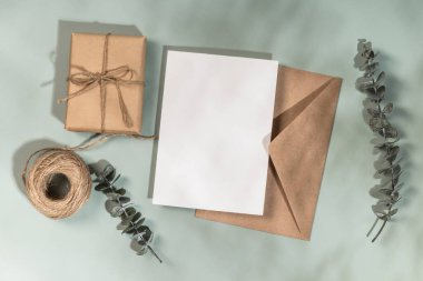 Tebrik kartı ya da düğün davetiyesi modeli. Kraft zarfı, boş antet, hediye kutusu ve zeytin arkaplanda okaliptüs dalları..