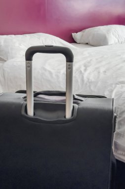 Otel odasında yeni yapılmış bir yatağın yanında siyah bir bavul..