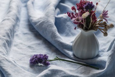 Kurumuş çiçekli seramik küçük vazo ve keten açık mavi masa örtüsü üzerinde bir tutam statik çiçek. Bahar narin çiçekli arka plan, seçici odak.