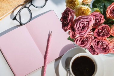 Şık bir iş yeri. Güller, defter, bardaklar ve bir fincan kahve..