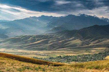 Güneşin gün batımı ışınları dağ vadisindeki bulutları delip geçer. Dağlarda güneşli bir gün batımı. Fırtınalı gökyüzü. Kırgızistan 'ın dağ manzaraları.
