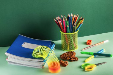 Yeşil arka planda not defterleri, kalemler ve diğer okul kağıtları. Öğrenci işyeri organizasyonu.