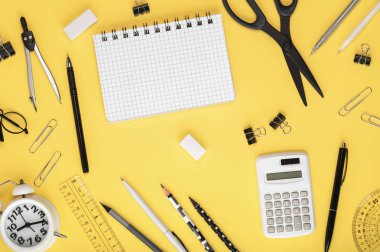 Siyah beyaz kırtasiye malzemesi, defter, çalar saat ve hesap makinesi sarı arka planda. Okul konseptine geri dönelim. Çalışma alanı organizasyonu.
