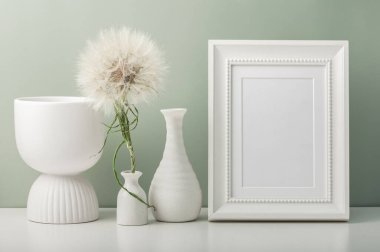 Boş bir fotoğraf çerçevesi, üç beyaz vazo ve masada bir karahindiba. Minimalist iç mekan.