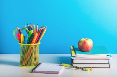 Bir yığın kitap, kalemler, kalemler ve mavi arka planda açık bir defter. Okula, öğretmenler gününe..