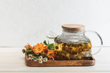 Çaydanlıkta taze demlenmiş papatya çiçeği çayı ve beyaz bir masada şifalı bitkiler. Organik doğal ilaç. Seçici odaklanma..