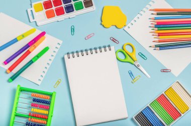 Okul konseptine geri dönelim. Renkli okul kırtasiyesi, çocuk abaküsü, renkli kalemler, işaretleyiciler ve açık boş defterli mavi arka planda daha fazlası..