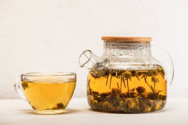 Çaydanlıkta taze demlenmiş papatya çayı ve beyaz bir masada bir fincan çay. Organik doğal ilaç..