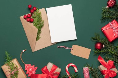 Yılbaşı kartı, geçmiş. Köknar dalları, Noel oyuncakları ve hediyeler çerçevesi. Yeşil arkaplanda zarf ve boş kart.