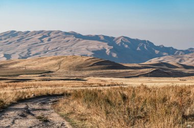Sonbaharda kuru çayırlar ve tepelerin arasında toprak bir yol. Kırgızistan 'da sakin bir sonbahar.