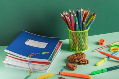 Okul kırtasiyesi, kalem tutacağı ve yeşil arka planda kopyalanmış kurabiyeler. İş yeri organizasyonu. Okula geri dön..