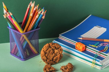 Defterler, kalem açacağı, kurabiyeler ve yeşil arka planda kalem tutacağı. İş yeri organizasyonu. Seçici odaklanma. Okula geri dön..