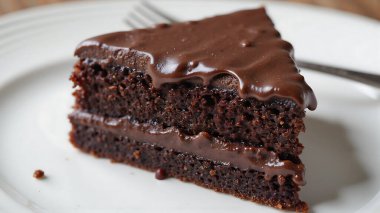 Bir dilim nemli çikolatalı pasta, kremalı krema katmanlı temiz beyaz tabakta duruyor, sıcak bir tatlı toplantısında tadını çıkarmaya hazır, tatlı aşermeler için mükemmel..