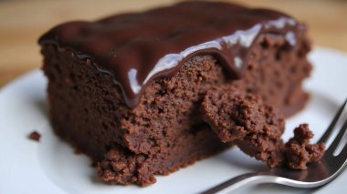 Çürümüş bir çikolatalı pasta beyaz bir tabakta sergileniyor, içinde parlak çikolatalı krema var. Yanına bir çatal konur, keyiflenmeye hazır lezzetli bir ziyafeti işaret eder..