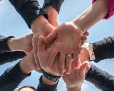 Birbirinin üzerine istiflenmiş ellerin HA 'daki sembolik görüntüsü takım çalışmasını, birliği ve işbirliğini sembolize ediyor. Yakın çekim bir grubun çeşitliliğini ve kolektif gücünü vurgular