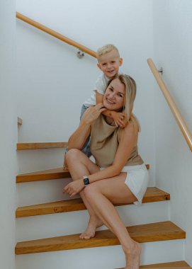 Mutlu anne ve 3 yaşındaki oğlu evin kenarlarında beyaz duvarlarla evlerinin merdivenlerinde oturuyorlar. Yüksek kalite fotoğraf