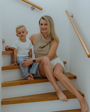 Mutlu anne ve 3 yaşındaki oğlu evin kenarlarında beyaz duvarlarla evlerinin merdivenlerinde oturuyorlar. Yüksek kalite fotoğraf