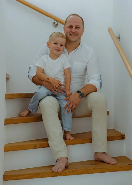 happy dad and 3 year old son sitting on the stairs in their house with white walls on the sides of the house. High quality photo