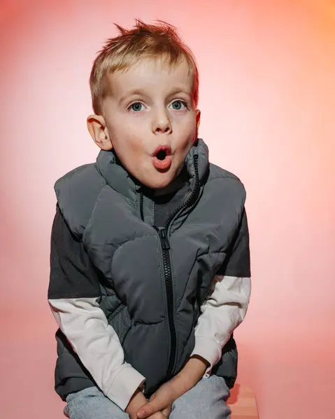 portrait of a surprised boy looking directly at the camera in a shirt and shorts against a gray background . High quality photo