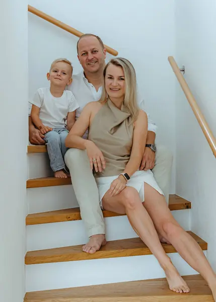 happy dad mom and 3 year old son sitting on the stairs in their house with white walls on the sides of the house. High quality photo