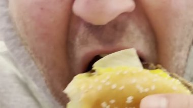 Bir adamın ağzı hamburger çiğneyip ağzını yalıyor. Yüksek kaliteli FullHD görüntüler