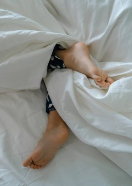 Küçük bir çocuğun ayakları beyaz çarşafların üzerinde beyaz bir battaniyeye sarılmış bir ebeveyn yatağında. Yüksek kalite fotoğraf