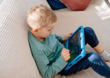 4 yaşındaki bir çocuk elinde tabletle evdeki kanepede oturuyor. Yüksek kalite fotoğraf