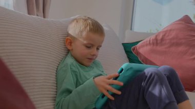 4 yaşındaki bir çocuk elinde tabletle evdeki kanepede oturuyor. Yüksek kalite fotoğraf