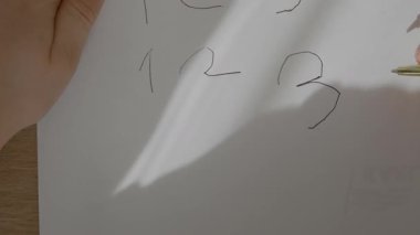 Bir çocuk rakamları beyaz kağıda yazmayı öğrenir, altın bir kalemi tutan bir çocuğun eline yakın plan yapmayı ve hayattaki ilk numaralarını yazmayı. Yüksek kalite 4k görüntü