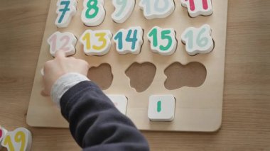 Çocuk saymayı öğreniyor, 1 'den 20' ye kadar sıralanmış sayı bulmacalarıyla dolu bir tahtayı tutuyor, çocuk 4-5 yaşında Avrupa görünümlü, evde oturuyor, okula hazırlanıyor. Yüksek