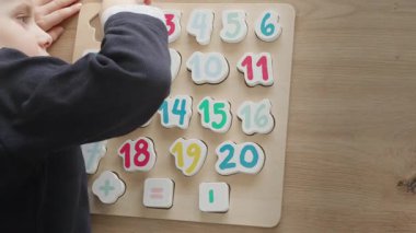 Çocuk saymayı öğreniyor, 1 'den 20' ye kadar sıralanmış sayı bulmacalarıyla dolu bir tahtayı tutuyor, çocuk 4-5 yaşında Avrupa görünümlü, evde oturuyor, okula hazırlanıyor. Yüksek