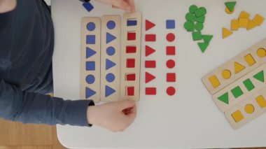 Çocuk kırmızı ve mavi ahşap geometrik şekilleri dikkatlice düzenler daire, kare, üçgen ve dikdörtgen masa üzerinde onları şekil sıralayarak. Montessori 'den esinlenilmiş harika bir öğrenme deneyimi
