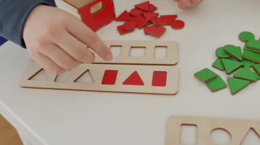 Çocuk dikkatlice kırmızı ahşap şekilleri düzenler daire, kare, üçgen ve dikdörtgen masanın üzerinde, onları şekillerine göre sıralar. Montessori 'den esinlenilmiş harika bir öğrenme deneyimi. Yüksek kalite