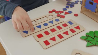 Çocuk kırmızı ve mavi ahşap geometrik şekilleri dikkatlice düzenler daire, kare, üçgen ve dikdörtgen masa üzerinde onları şekil sıralayarak. Montessori 'den esinlenilmiş harika bir öğrenme deneyimi