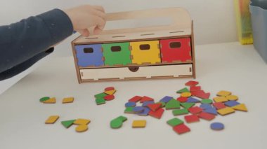 Küçük öğrenci, çok renkli geometrik şekilleri karşılık gelen kutulara yerleştirir: kırmızı, sarı, yeşil ve mavi. Farklı renklerin geometrik şekilleri masanın üzerine saçılmıştır. Bu Montessori