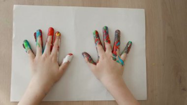 Çocuklar avuç içlerine boya bulaşmış, bir çocuk avuç içlerini bir kağıt parçasına, 4-5 yaşındaki bir çocuğun avuçlarını açık bırakarak bir iz bırakıyor. Yüksek kalite 4k görüntü